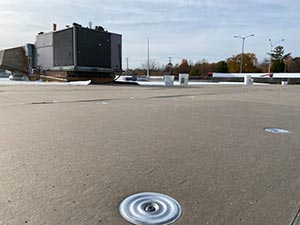 Rooftop with a large HVAC unit and ductwork, circular roof drain visible in the foreground under a blue sky