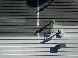 Roof-Coating-Bowling-Green-KY-Kentucky-1 | Glick Roofing Systems Two workers on a metal rooftop, one wearing a yellow helmet, performing maintenance on the panels with long shadows cast below them.
