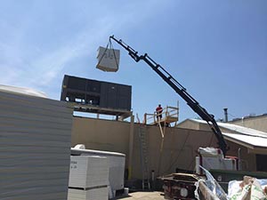 Single-Ply-Roofers-Nashville-TN-Tennessee-1 | Glick Roofing Systems Crane with a long arm hoisting a large HVAC unit onto the roof as two workers guide it from a platform.