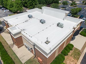 Single-Ply-Roofing-Bowling-Green-KY-Kentucky-1 | Glick Roofing Systems Aerial view of a brick commercial building with a white flat roof and multiple rooftop HVAC units; surrounding parking lot and greenery.