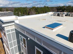 TPO-Roof-Repair-Nashville-TN-Tennessee-1 | Glick Roofing Systems Rooftop view of a white flat roof with a blue skylight, HVAC units, and a glass-windowed facade, under a blue sky with trees in the distance.